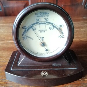 May include: A black Bakelite thermometer with a white face and black markings. The thermometer reads from 30 to 100 degrees Fahrenheit and has a comfort zone marked on the face. The thermometer is made by the British Rototherm Co. Ltd. and has an RCA logo on the base.