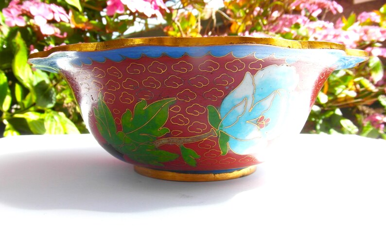 May include: A red and blue cloisonn&eacute; bowl with a floral design. The bowl has a scalloped rim and a gold trim.
