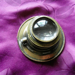 May include: A brass magnifying glass with a round lens and a decorative rim. The lens is clear and reflects the surrounding environment.