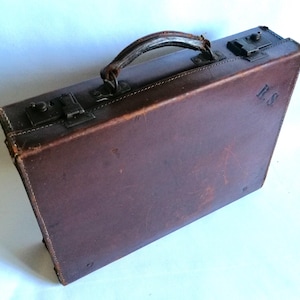 May include: A brown leather briefcase with a metal handle and clasps. The briefcase has a worn look and the initials "K.S." are embossed on the side.