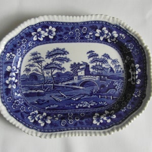 May include: A blue and white oval serving platter with a blue and white floral border and a central scene of a bridge over a river with trees and a building in the background.