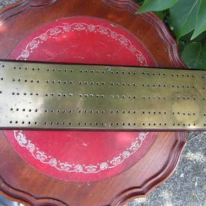 May include: A vintage brass peg board game with a dark brown wooden frame. The board is rectangular and has evenly spaced holes.