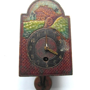 May include: A vintage wooden clock with a painted scene of a house and a water wheel. The clock face is black with white Roman numerals and gold hands. The clock has a pendulum and is hanging from a hook.