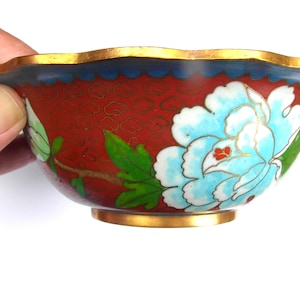 May include: A red cloisonn&eacute; bowl with a blue and white floral design. The bowl has a scalloped rim and a gold trim.