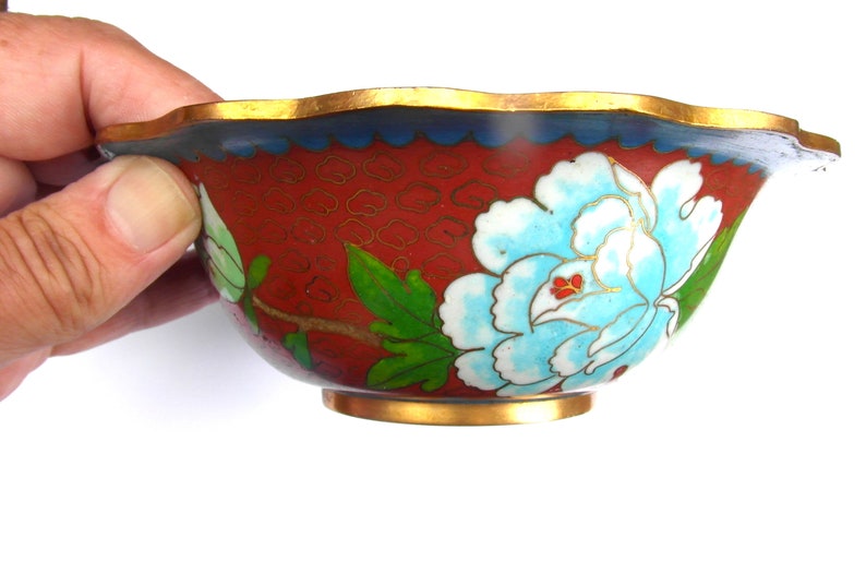 May include: A red cloisonn&eacute; bowl with a blue and white floral design. The bowl has a scalloped rim and a gold trim.