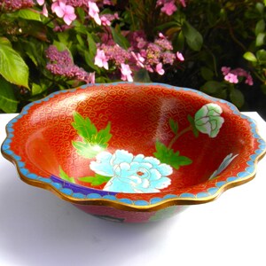 May include: A red cloisonn&eacute; bowl with a scalloped rim and floral designs in blue, green, and white.
