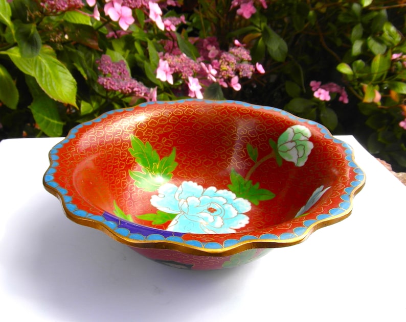 May include: A red cloisonn&eacute; bowl with a scalloped rim and floral designs in blue, green, and white.