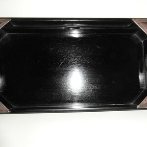 May include: A black lacquered serving tray with silver corners. The tray has a smooth, polished surface.
