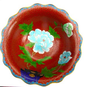May include: A red and blue cloisonn&eacute; bowl with a scalloped rim. The bowl is decorated with a floral pattern of white and blue peonies and green leaves.