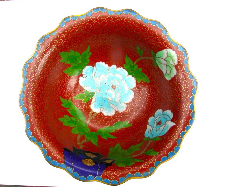 May include: A red and blue cloisonn&eacute; bowl with a scalloped rim. The bowl is decorated with a floral pattern of white and blue peonies and green leaves.