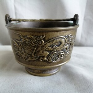 May include: A small, brass incense burner with a dragon design. The burner has a handle and a round base.