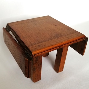 May include: A small wooden drop leaf table with a brown finish. The table has two leaves that can be folded down to make it smaller.