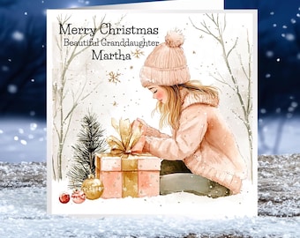 Può includere: Un biglietto di auguri di Natale con una ragazza con un cappello e un cappotto rosa che apre una scatola regalo con un nastro dorato. Il biglietto ha il testo "Merry Christmas Beautiful Granddaughter Martha".