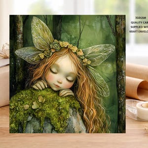 May include: A square greeting card with an illustration of a sleeping fairy with auburn hair, a floral crown, and large, delicate wings. The fairy rests on a mossy surface against a green forest backdrop. Supplied with a kraft envelope.