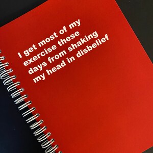 May include: A red spiral bound notebook with the text "I get most of my exercise these days from shaking my head in disbelief" printed in white.