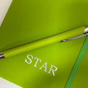 May include: A bright green notebook with a silver pen and the word "STAR" printed on the cover.