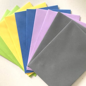 May include: A stack of colourful envelopes in shades of green, yellow, blue, purple, and grey. The envelopes are arranged in a fan shape.