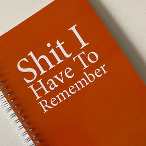 May include: Orange spiral bound notebook with the text "Shit I Have To Remember" in white.