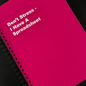 May include: A pink spiral bound notebook with the text "Don't Stress - I Have A Spreadsheet" printed in white.