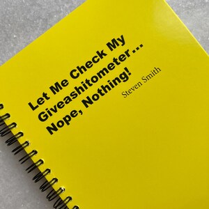 May include: A bright yellow spiral-bound notebook with black text that reads "Let Me Check My Giveashitometer... Nope, Nothing!" and the name "Steven Smith." The notebook has a glossy cover.