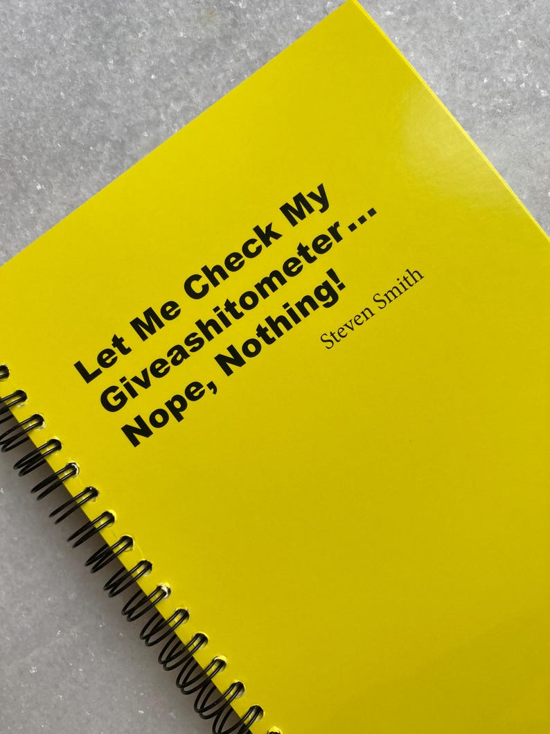 May include: A bright yellow spiral-bound notebook with black text that reads "Let Me Check My Giveashitometer... Nope, Nothing!" and the name "Steven Smith." The notebook has a glossy cover.