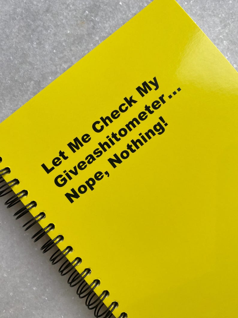 May include: A bright yellow spiral-bound notebook with black text that reads "Let Me Check My Giveashitometer... Nope, Nothing!" The notebook is open, displaying the glossy cover. The spiral binding is black.