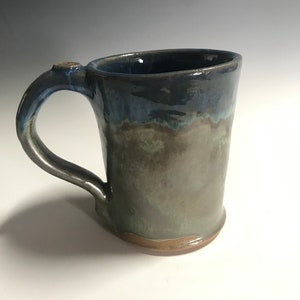 May include: A handmade ceramic mug with a blue and green glaze. The mug has a rounded body and a handle.