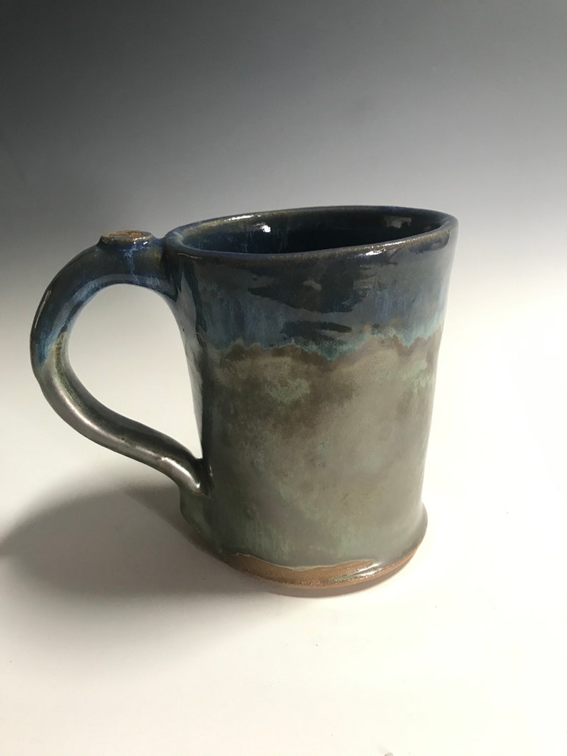 May include: A handmade ceramic mug with a blue and green glaze. The mug has a rounded body and a handle.