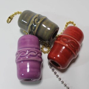 May include: Three ceramic fan pull chains with decorative designs. The chains are gold and the pulls are purple, red, and green.