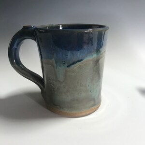 May include: A handmade ceramic mug with a blue and green glaze. The mug has a rounded body and a handle.