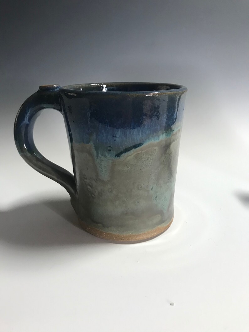 May include: A handmade ceramic mug with a blue and green glaze. The mug has a rounded body and a handle.