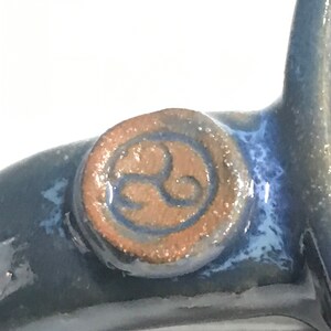 May include: Close-up of a blue ceramic mug with a brown and blue circular logo featuring a stylized symbol.
