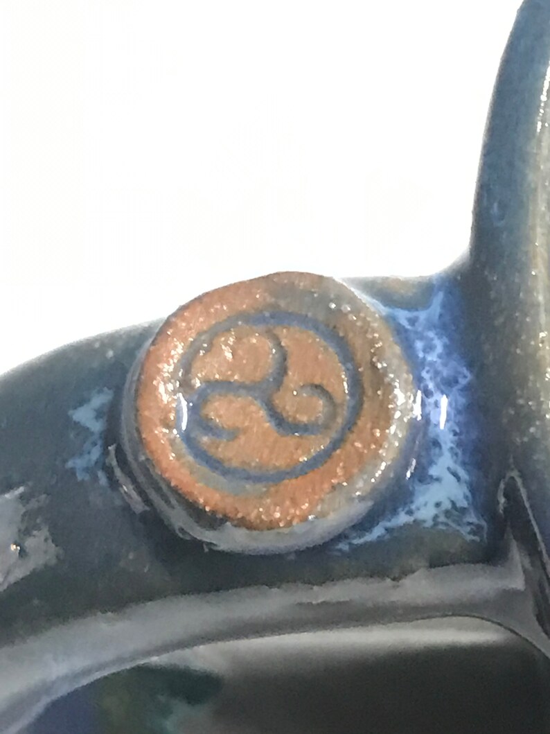 May include: Close-up of a blue ceramic mug with a brown and blue circular logo featuring a stylized symbol.