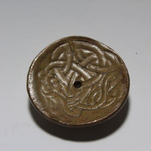 May include: A brown ceramic dish with a Celtic knot design. The dish has a small hole in the center.