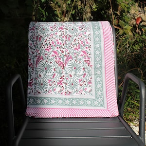 May include: A white cotton throw blanket with a pink and green floral pattern. The blanket is folded and placed on a black metal chair.