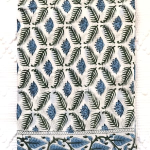May include: White cotton fabric with a blue and green floral print. The fabric has a border with a repeating pattern of blue leaves and stems.