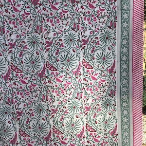 May include: White fabric with a pink and green floral pattern. The fabric has a border with a repeating floral design.