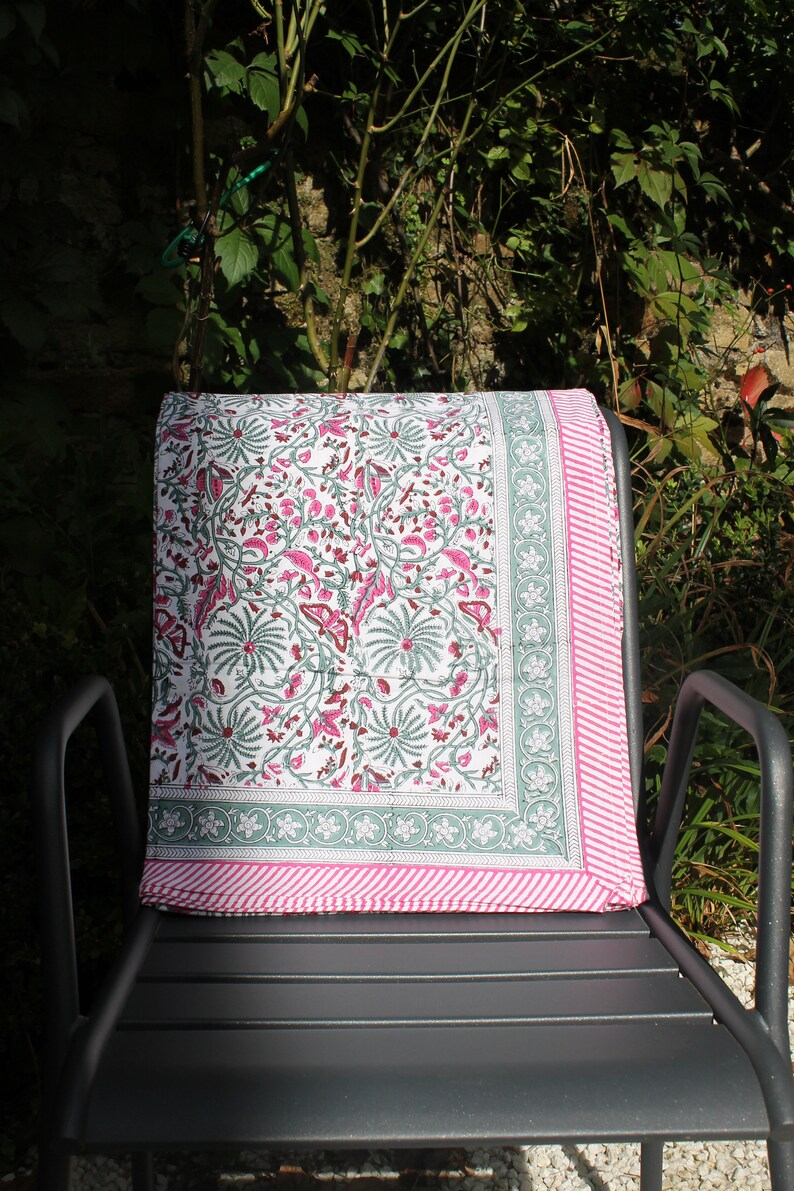 May include: A white cotton throw blanket with a pink and green floral pattern. The blanket is folded and placed on a black metal chair.