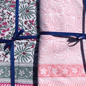 May include: Two fabric squares tied together with blue ribbon. One square has a white background with pink floral patterns. The other square has a white background with green and pink floral patterns.