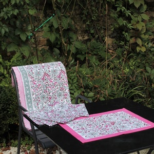 May include: A black metal table with a pink and white floral patterned tablecloth and matching placemats. The table is set up outdoors with a chair in the background.