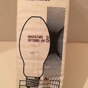May include: A vintage Philips MasterColor Metal Halide light bulb box. The box is white with red accents and features a black line drawing of a light bulb. The text "MANUFACTURED SEPTEMBER 1997" is printed on the bulb. The Philips logo is at the top.