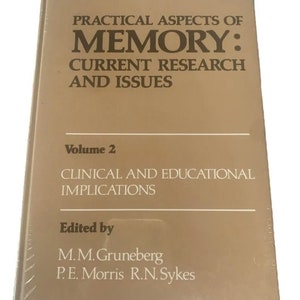 May include: A book titled "Practical Aspects of Memory: Current Research and Issues, Volume 2." The cover is a light brown colour with the title and author's names in dark brown. The book is sealed in clear plastic.