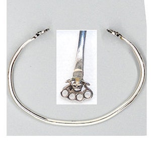 May include: A silver bangle bracelet with a decorative design on the clasp. The design features a stylised face with three circles on each side.