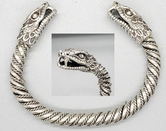 May include: Silver bracelet with two snake head ends. The bracelet is made of twisted silver wire and the snake heads are detailed with scales and fangs.