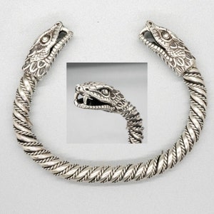 May include: Silver bracelet with two snake head ends. The bracelet is made of twisted silver wire and the snake heads are detailed with scales and fangs.
