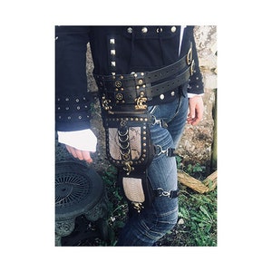 Könnte beinhalten: Ein schwarzer Ledergürtel mit einer großen Metallschnalle und einem Oberschenkelholster mit Schlangenhautmuster. Das Holster hat einen Reißverschluss und mehrere Metallringe.