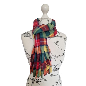 May include: A vibrant, fringed scarf in a plaid pattern, draped on a mannequin. The scarf showcases a mix of red, green, yellow, and orange squares. The fringing detail adds a tactile element to the design.