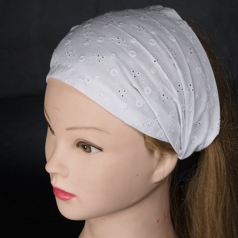May include: White cotton headband with a delicate eyelet pattern. The headband is wide and has a soft, stretchy feel.