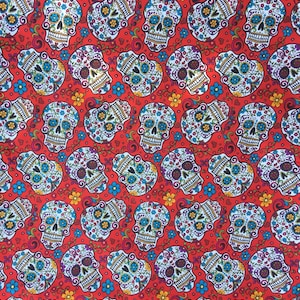 May include: Red fabric with a repeating pattern of white sugar skulls with colorful floral designs. The skulls have blue eyes and are surrounded by small red hearts and flowers.