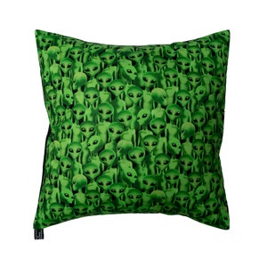 May include: Green pillow with a pattern of many alien faces.